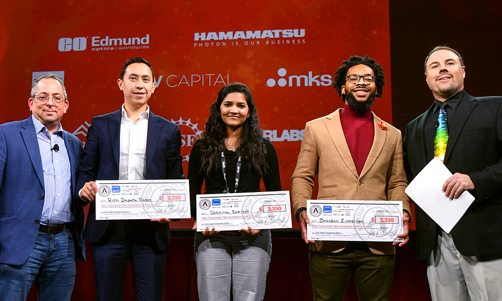 Business plan competition winners hold checks onstage