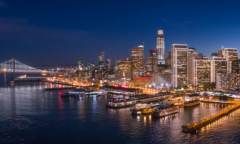 The San Francisco waterfront in the evening, lit up by the city lights and a peak of the Bay Bridge on the right