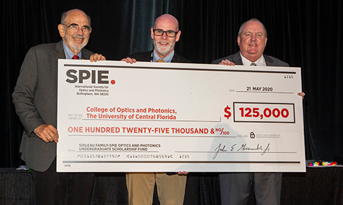 A picture of three people holding up a large check for $125,000, for the College of Optics and Photonics, The University of Central Florida