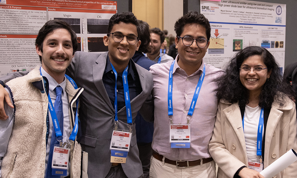 Three males and a female stand in front of poster presentations at SPIE Photonics West